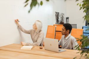 Two professionals collaborating at a startup office with a whiteboard and laptop