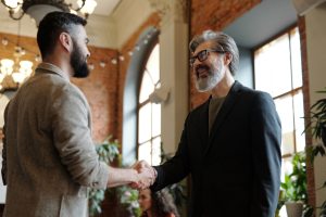 Two businessmen smiling during a handshake in a modern office setting, symbolizing success and partnership