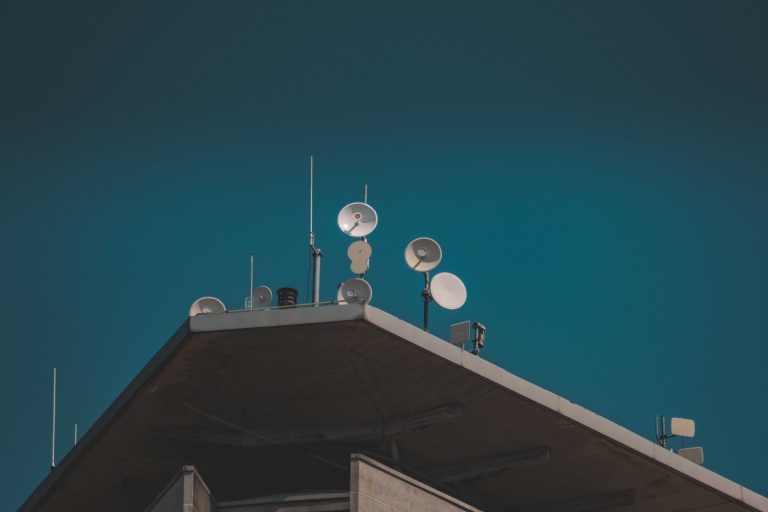 A low-angle view of communication dishes and antennas on a building against a clear blue sky