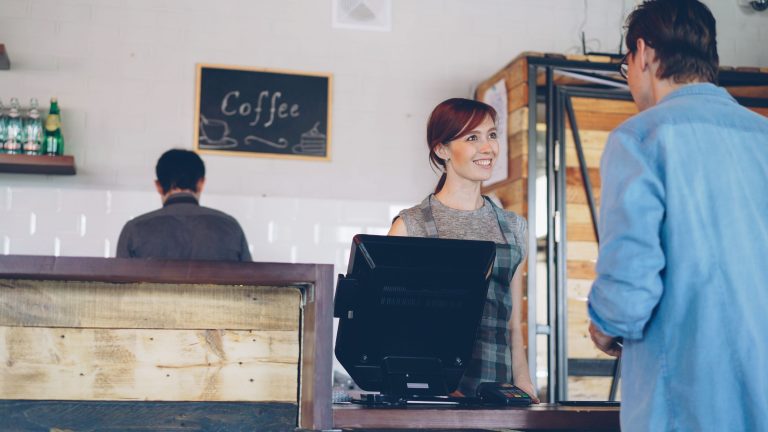 A smiling barista assists a customer at a coffee shop counter, creating a warm atmosphere