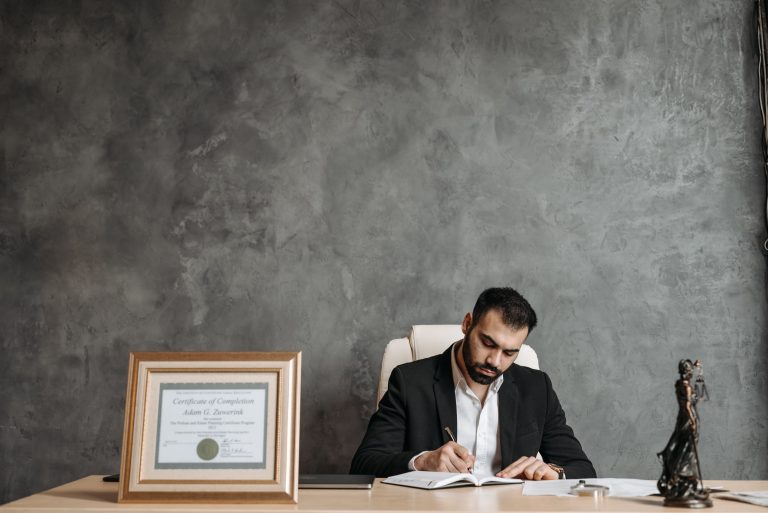 Person writing at a desk beside a justice statue