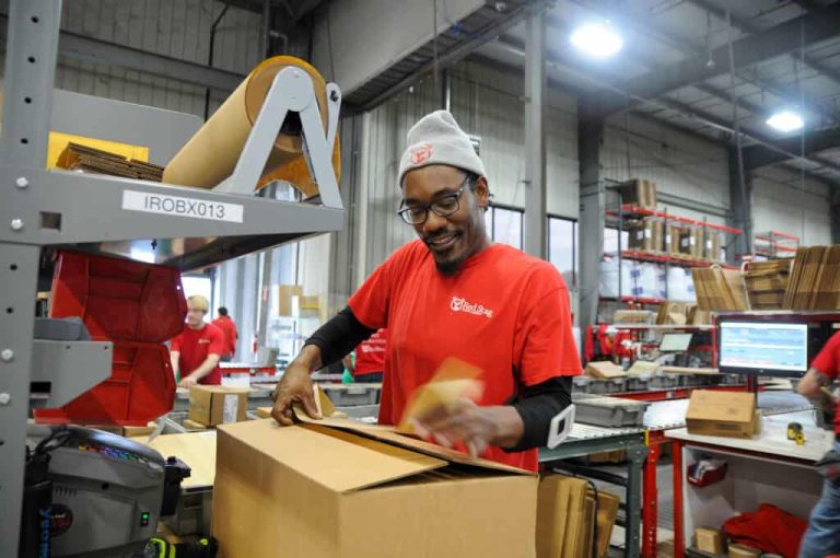 Warehouse worker packing a box among fulfillment equipment