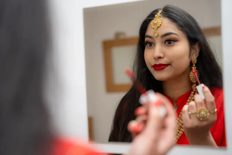 Sophisticated woman in traditional jewelry applying makeup in front of a mirror