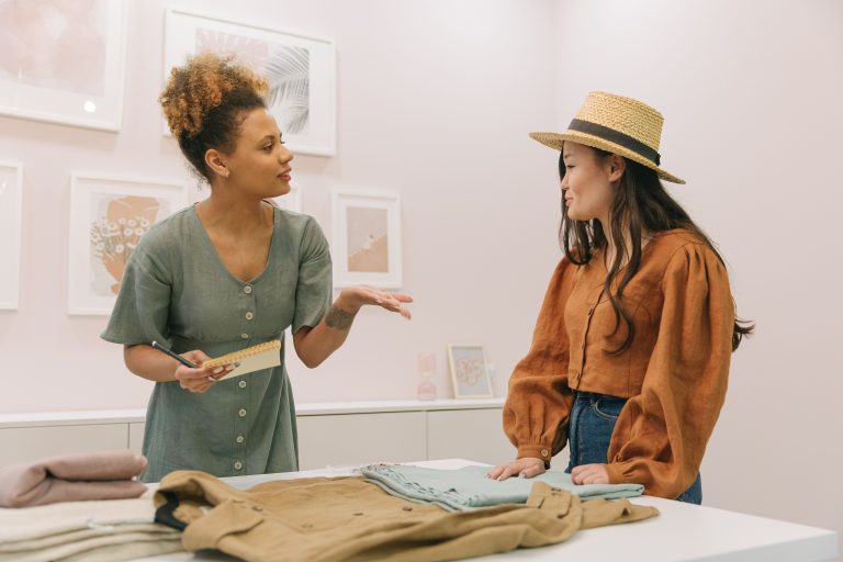 Two women discuss clothing designs at a worktable