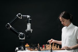 Illustrative photo of a robotic arm beside a person playing chess