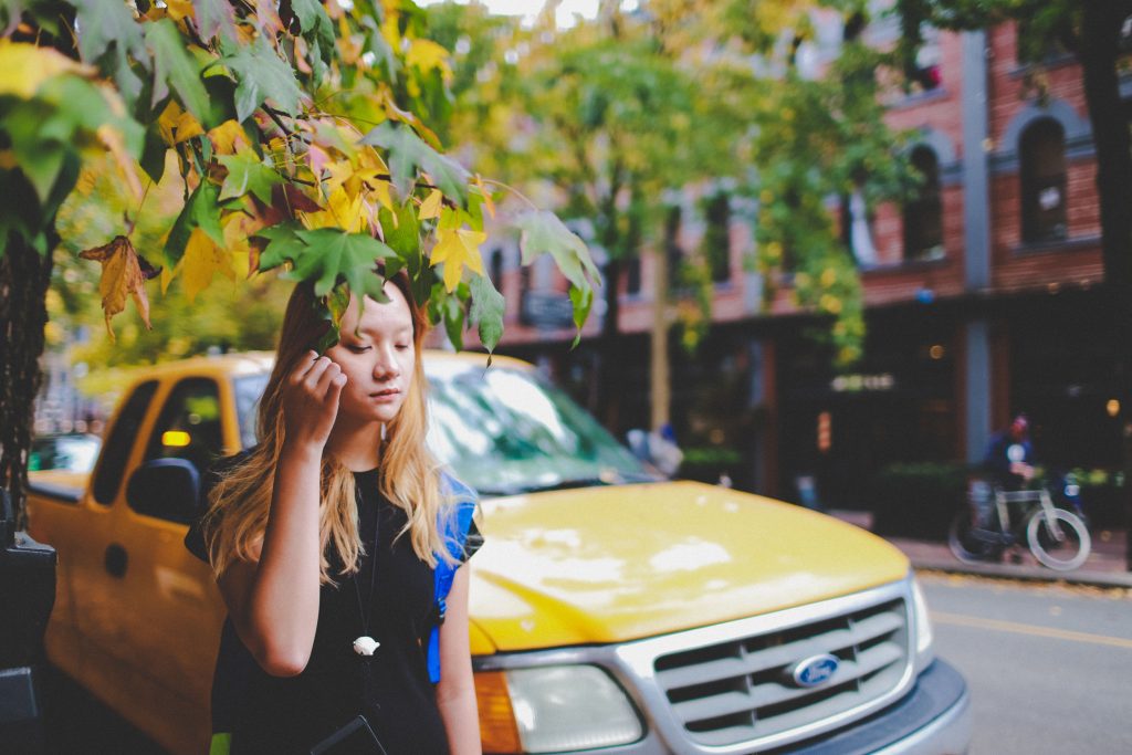 Woman standing in urban Vancouver street with autumn leaves and a yellow car in the background
